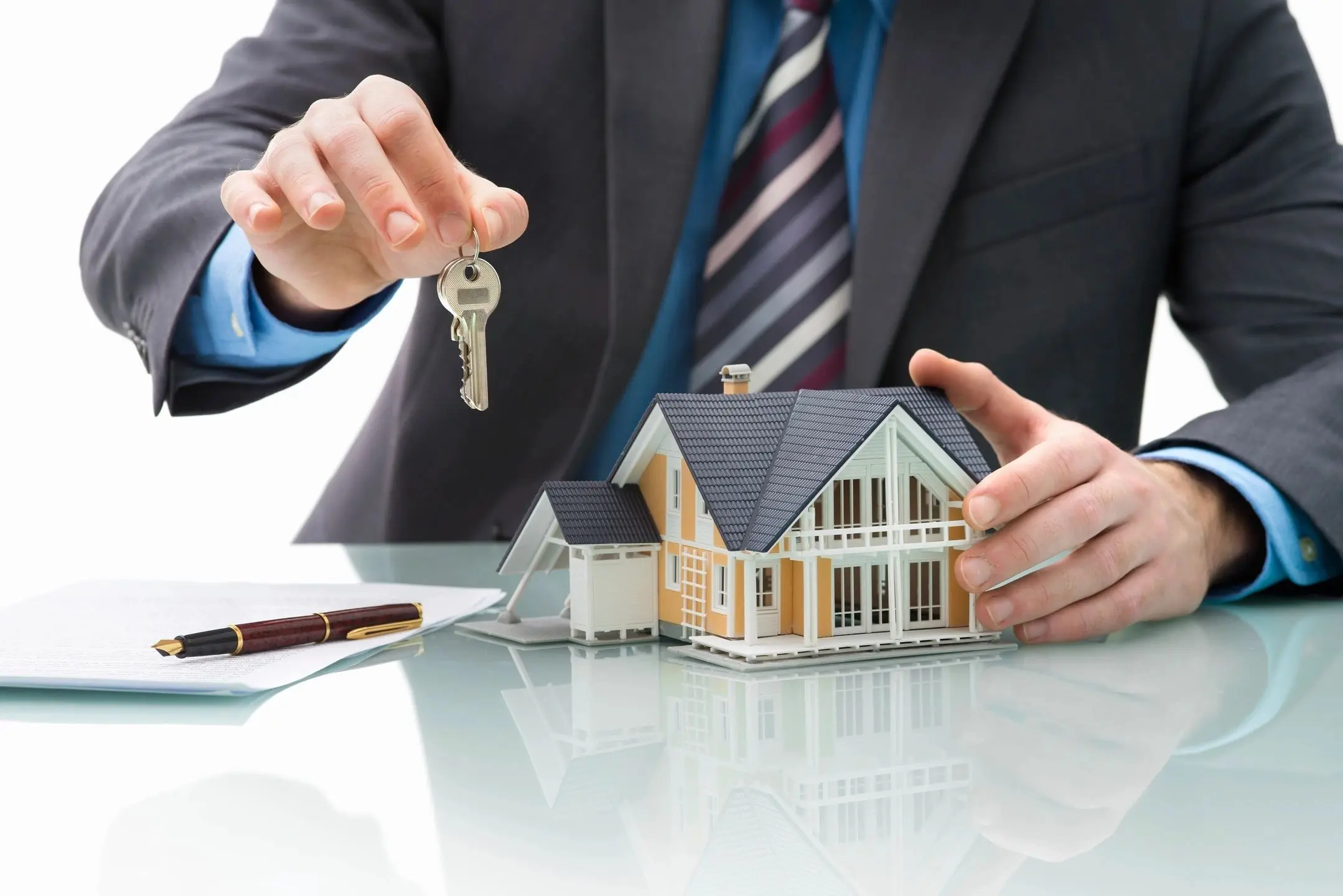 A man in a suit holding out keys to a house.